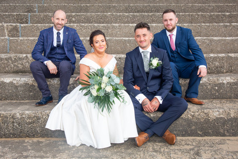 groomsmen and bride sat on steps at swansea bay
