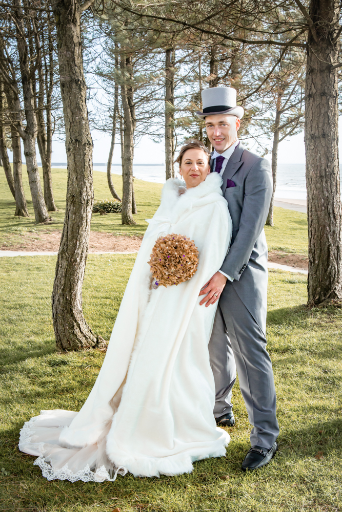 bride and groom stand for a photo on Swansea bay
