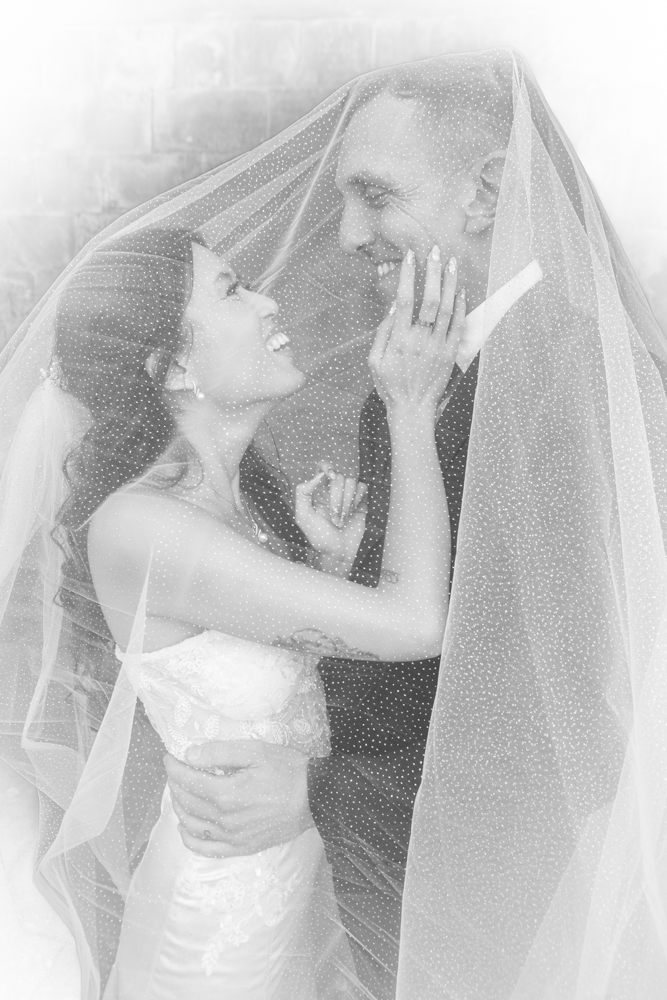 Bride and groom pose under the veil outside in dinefwr parc