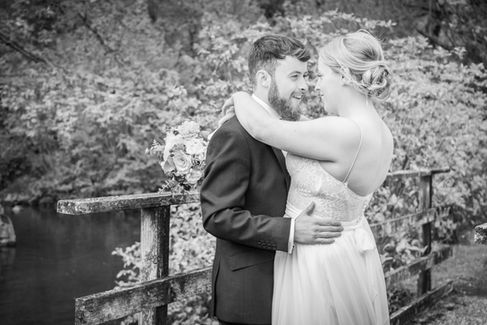 bride and groom hug on a small bridge next to a pond