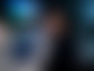 Mulher sorridente em reunião corporativa, com laptop mostrando painel de RH; tela ao fundo e colegas desfocados.