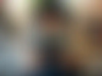 Mulher sorrindo atrás do balcão de um bar ou cafeteria, usando avental e segurando um tablet para controle de pedidos ou estoque, com garrafas de bebidas e máquina de café ao fundo.