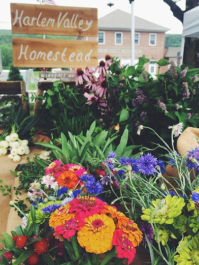 farmers market stand with flowers in the foreground and produce in wooden crates