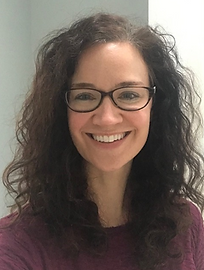White woman with dark curly hair and glasses, smiling.