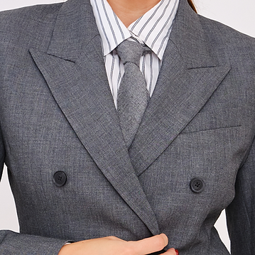 A round-framed, close-up photo of a woman in a striped collared shirt, a gray tie, and a matching gray double-breasted suit jacket, buttoning her jacket with the overlay text "6 years in business"
