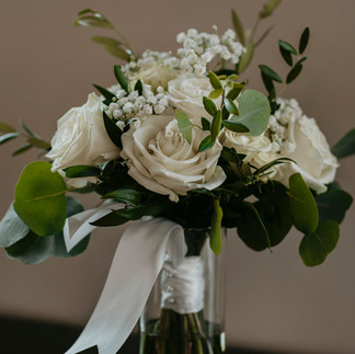bride's fresh floral bouquet featuring off white roses and greenery, tied with silk ribbons