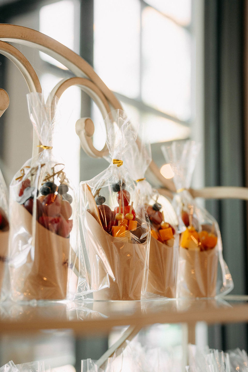 charcuterie cups wrapped in plastic for guests to enjoy placed on glass baker's rack shelves