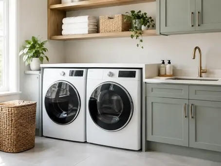 Modern laundry room with sage green cabinetry, front-loading washer and dryer, utility sink, countertop, and open shelving.