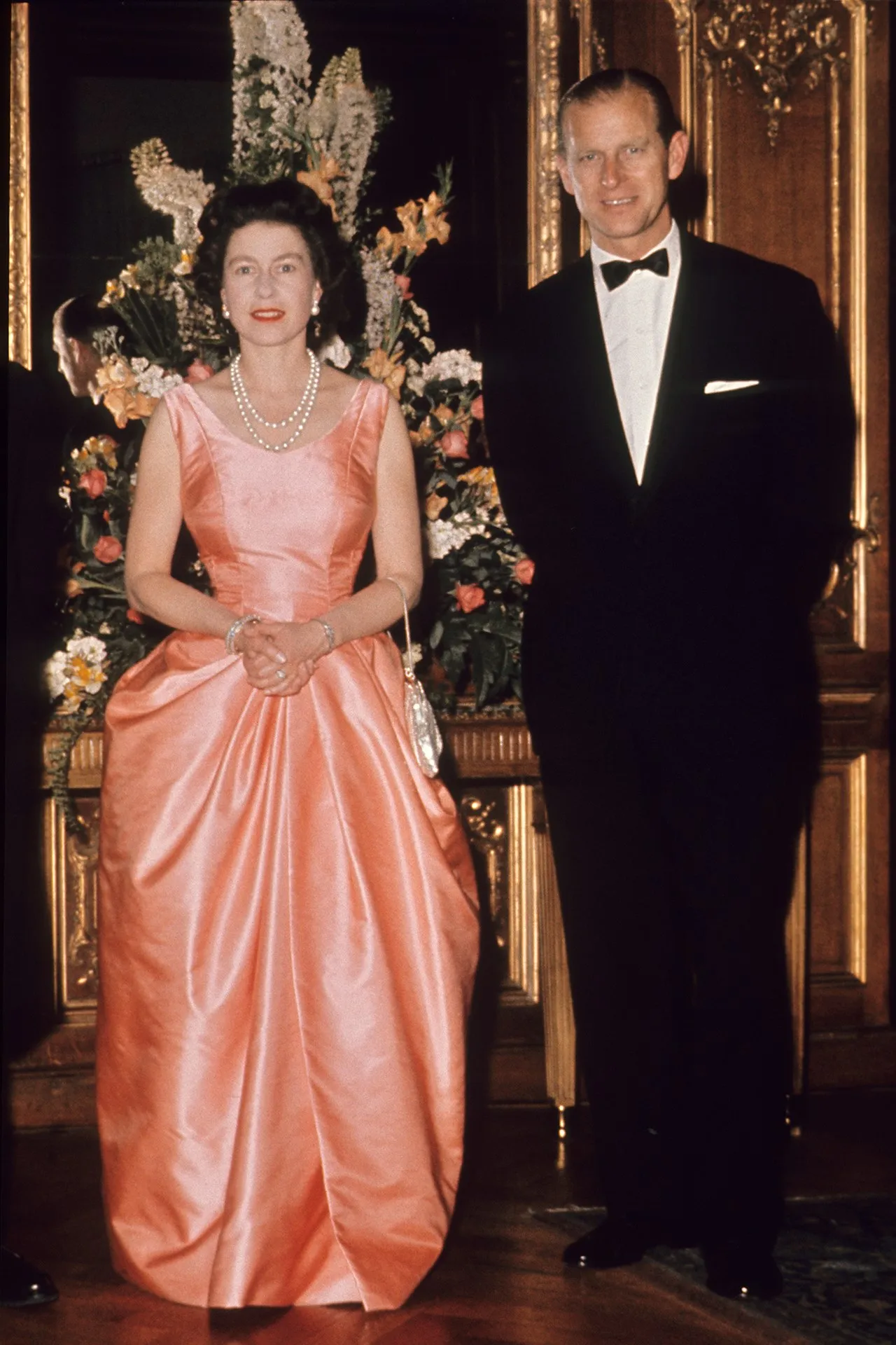The Queen and Prince Phillip attending an event in London in 1963. The Queen is wearing a coral evening dress and pearls.