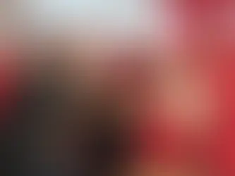 Um grupo de homens sorri e faz sinal de positivo com os polegares levantados, em um ambiente iluminado por luz natural. No centro da cena está Nico Acampora, fundador do projeto PizzAut, vestindo camisa branca e avental vermelho com o logo da pizzaria inclusiva. Ele segura uma pizza sobre uma bandeja de madeira, ladeado por jovens autistas que fazem parte da equipe do restaurante. Todos usam uniformes vermelhos com detalhes da marca PizzAut, demonstrando orgulho e alegria. Um dos homens à esquerda veste uma jaqueta de couro preta e camiseta colorida, destacando-se dos demais uniformizados. A imagem transmite um forte sentimento de união, inclusão social e celebração, ilustrando o sucesso do modelo de empregabilidade desenvolvido por Acampora para jovens no espectro autista.