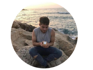 Oleh Jacob Feldman sitting on rocks along the sea