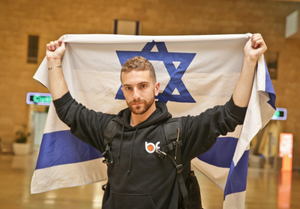 Oleh Simcha Brodsky in Ben Gurion Airport holding up an Israeli flag