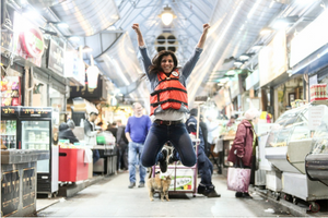 Orly Wahba wearing an orange life vest jumping with her arms raised inside the Mahane Yehuda Shuk