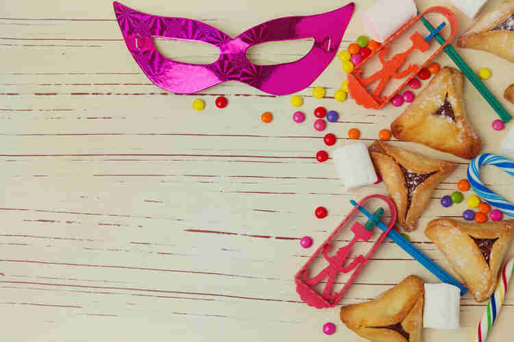 Table top covered in noisemakers, hamantaschen, candy, and a pink mask