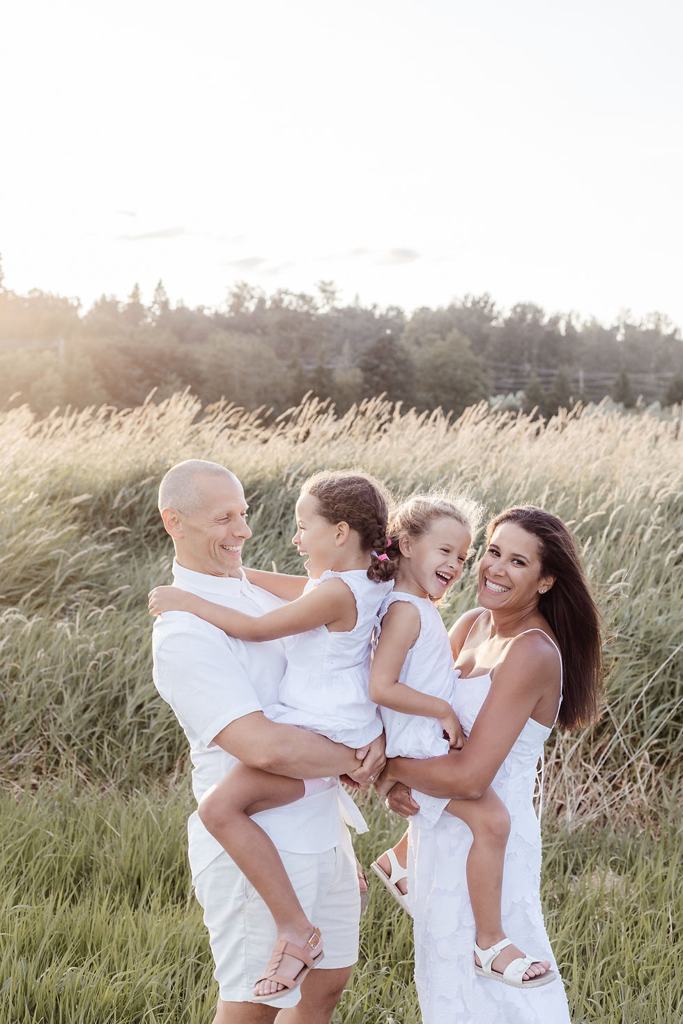 family of four smiling at sunset with golden light in long grass meadow in Abbotsford Willband Creek park with Meliza Orellana Photography