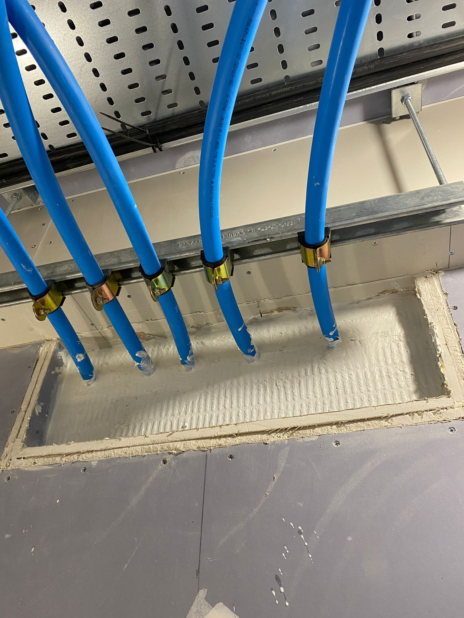 Grouped blue pipe penetrations at the wall head, Cobham firestopping project