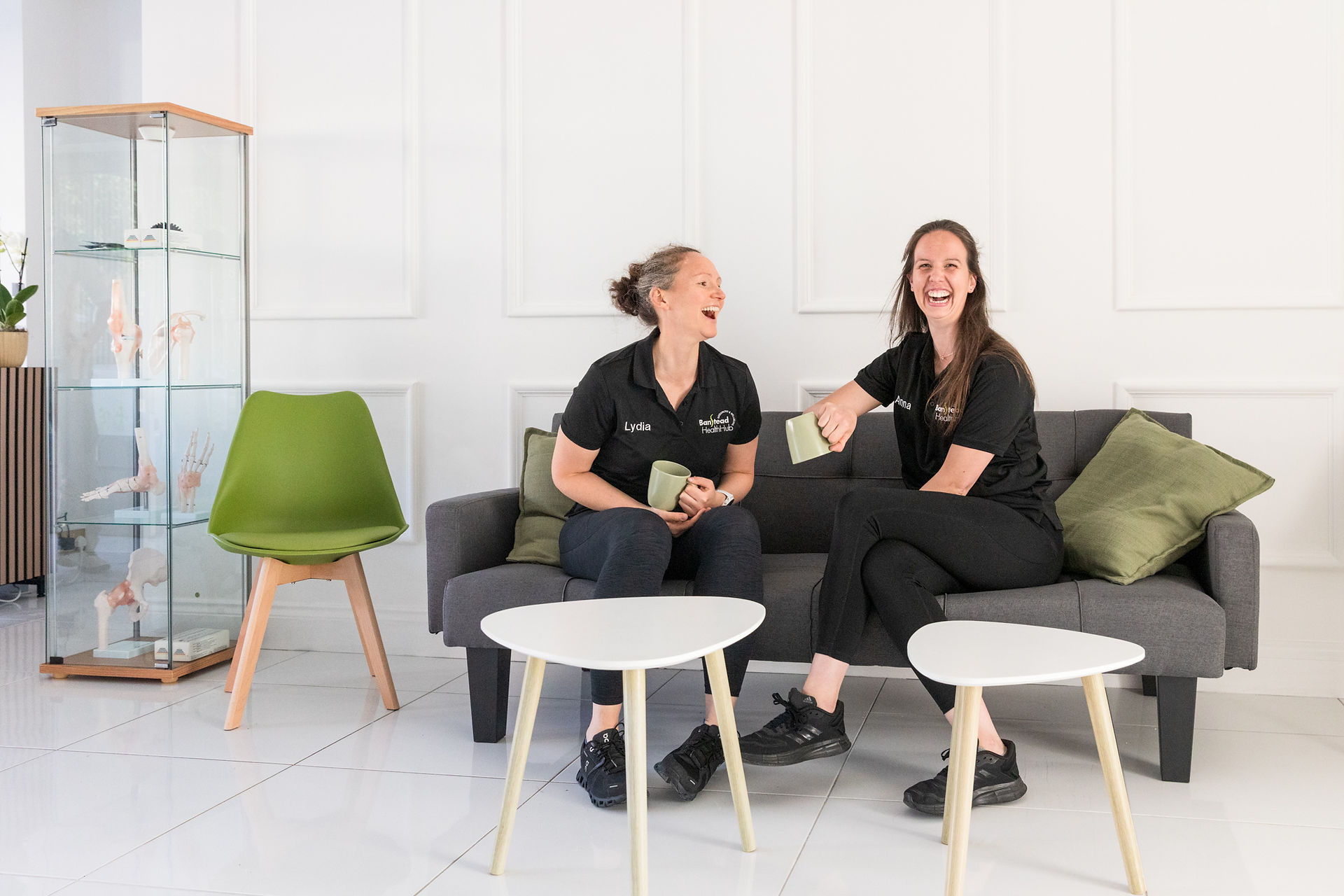 Osteopaths Lydia and Anna sitting on a sofa and laughing at Banstead Health Hub