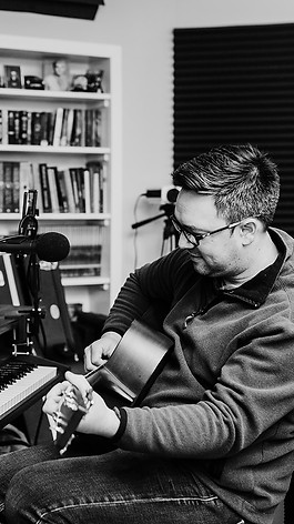 A man sits at a desk playing a guitar.