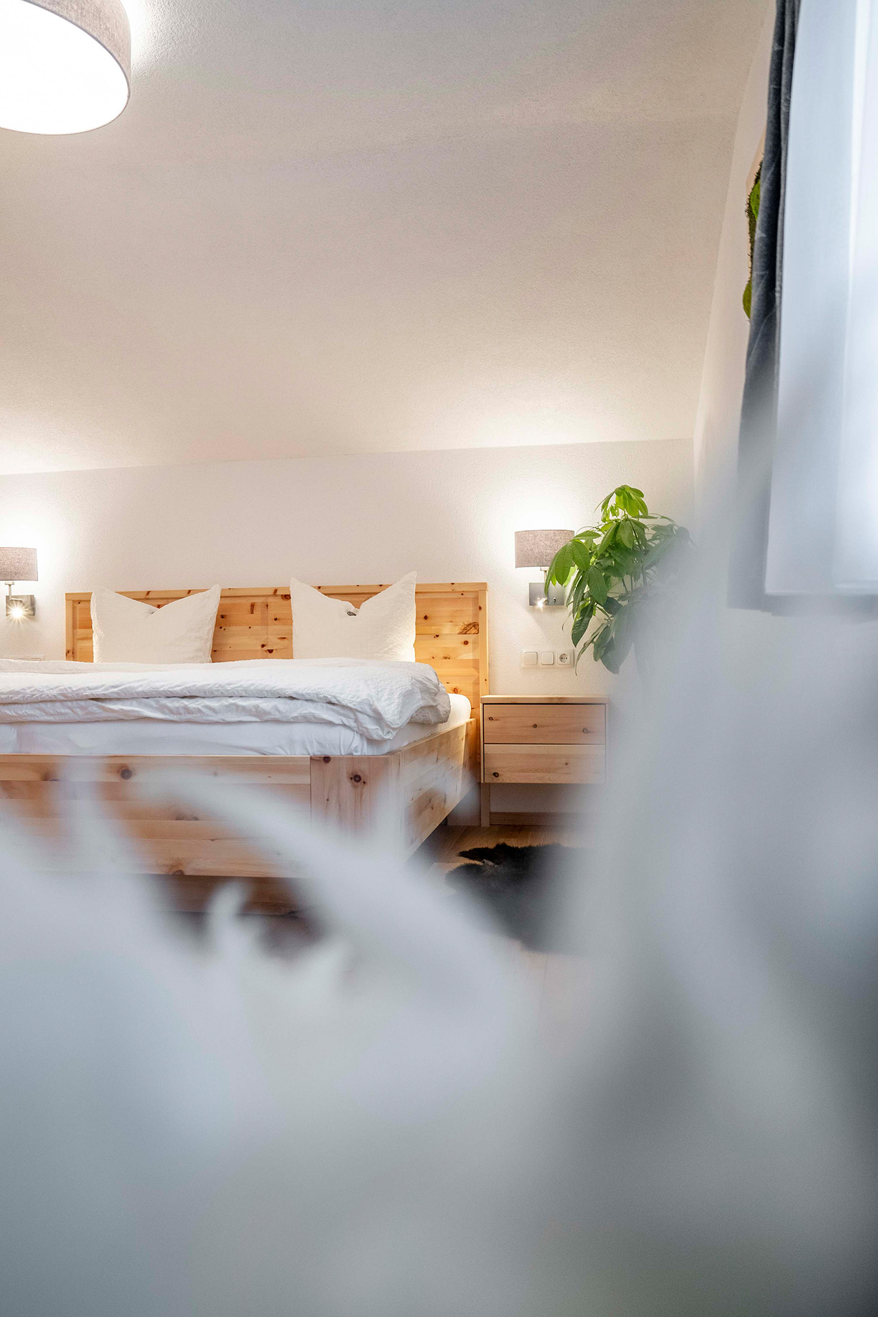 Zimmeransicht des Lofts von innen mit weißem Bettbezug und Pflanze neben dem Bett