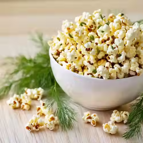 Bowl of Yummee Pop Dill Sea Salt & Vinegar popcorn surrounded by fresh dill, highlighting the bold, zesty flavor.