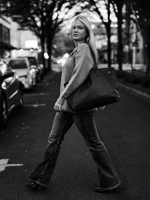 Blonde model crossing the street in denim jeans and a Prada Sweater in Downtown Eugene Oregon carrying a fashionable handbag