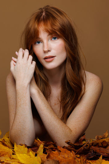 Red-haired woman with freckles, posing with fall leaves in studio. BEAUTY. Nick Johnson Photo