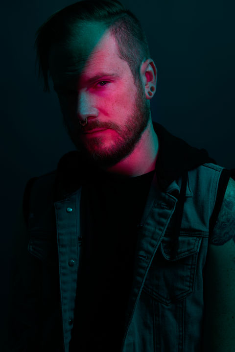 Bearded man in denim vest, dramatic lighting, EDITORIAL PORTRAITS, intense expression, Nick Johnson Photo