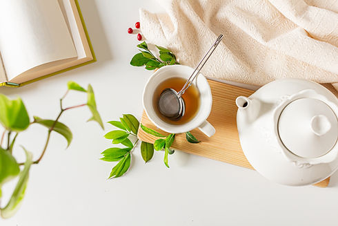 Cup of tea composition with tea strainer, tea pot,open book, cinnamon, plants green leaves