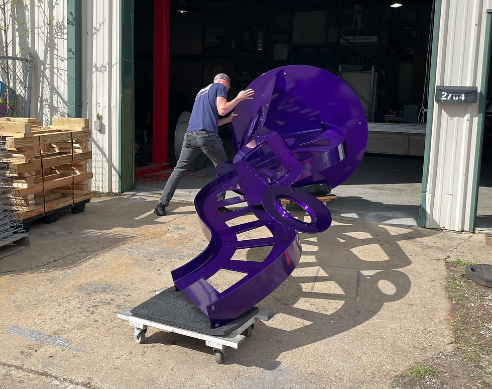 A white man wearing a navy blue t-shirt and black jeans guides a large purple sculpture into a warehouse.