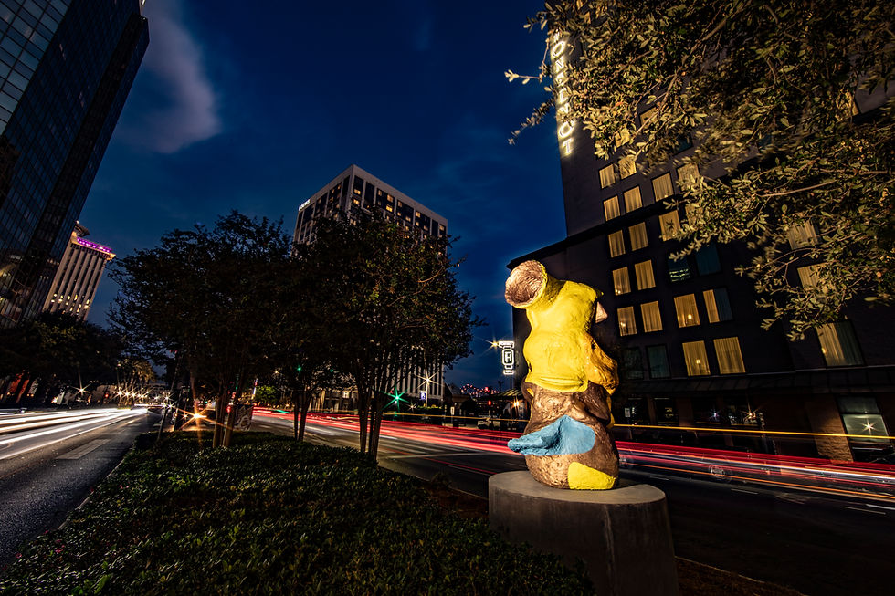 Arlene Shechet's yellow and gold 'Oomph' sculpture is illuminated at night on the Poydras Corridor of New Orleans. Office buildings and trees can be seen in the background.