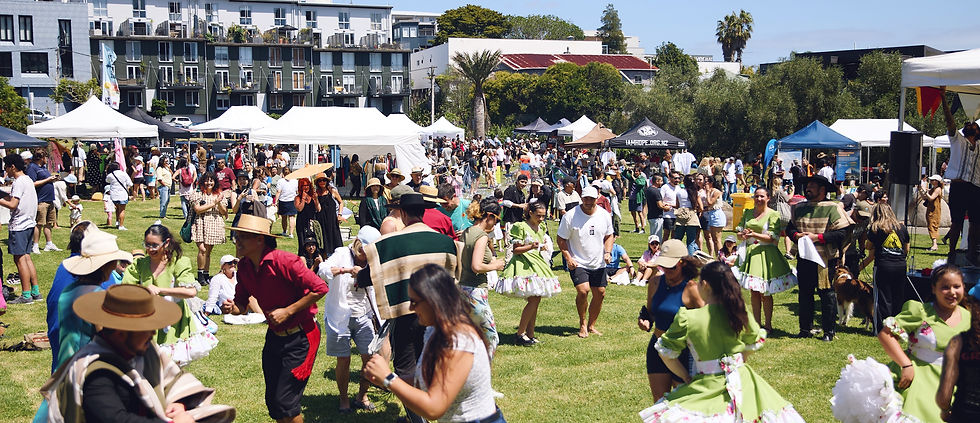 Crowd shot of event showing people dancing, the stage, stalls and food trucks in the distance