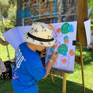 A young boy is drawing at an easel in the park