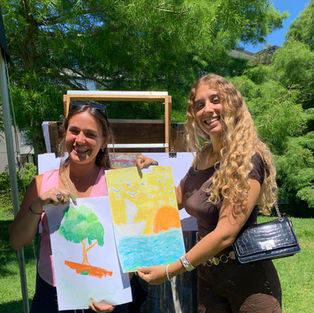 Two women hold up their drawings in front of the easels