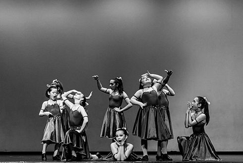 A young female dance performance group is shown on stage, in costumes.