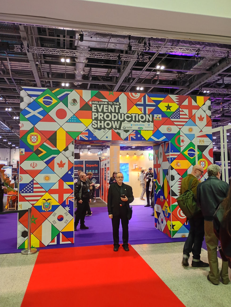 Visitors gather at the vibrant entrance of the Event Production Show, featuring a colorful display of international flags, creating an inviting atmosphere for industry experts and enthusiasts.