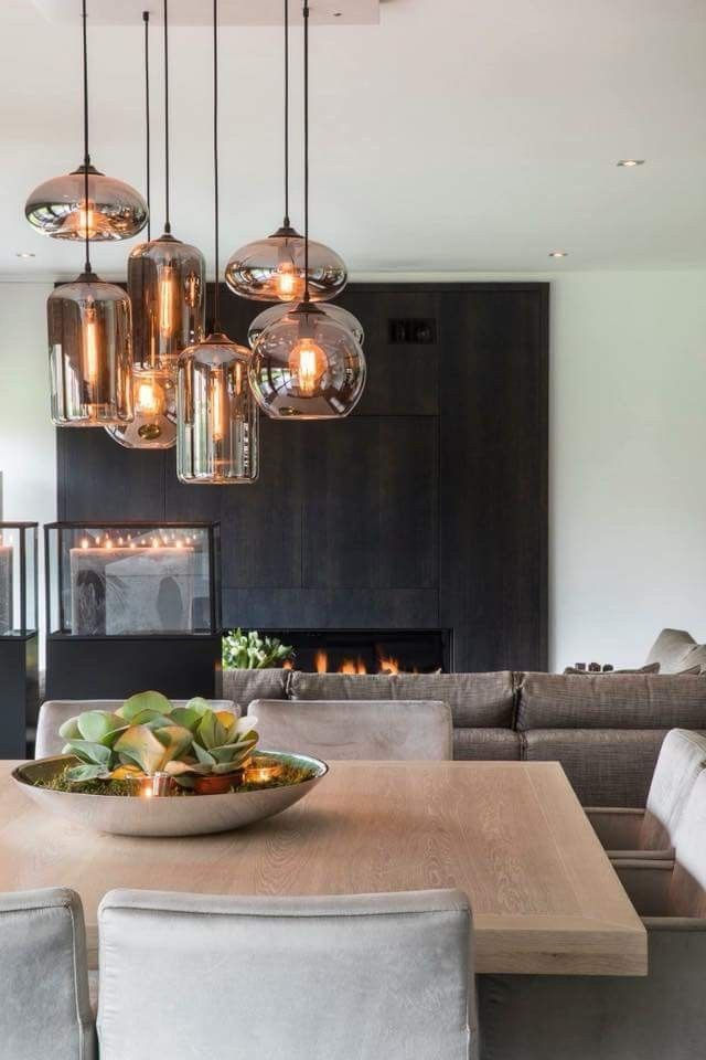 Modern dining room with hanging lights, fireplace and a wooden table. Nu Projects Dubai