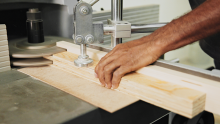 Person operating a band saw, cutting wood, industrial environment, close-up view.