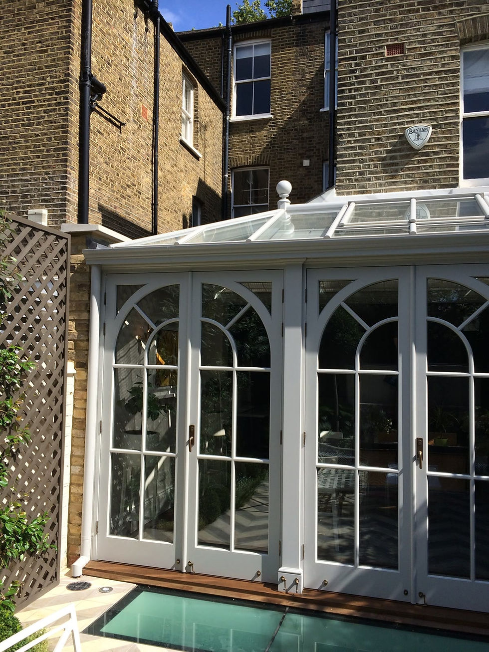 Painted timber orangery with arched glazing bars and a lantern roof against a London stock brick rear elevation with white sash windows