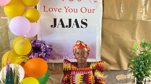 A Jaja, grandmother, is pictured here in a colorful dress in front of a sign that says, "We love you, our Jajas!"