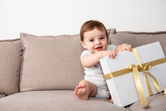 Baby houdt een witte geschenkdoos met gouden strik vast en lacht blij