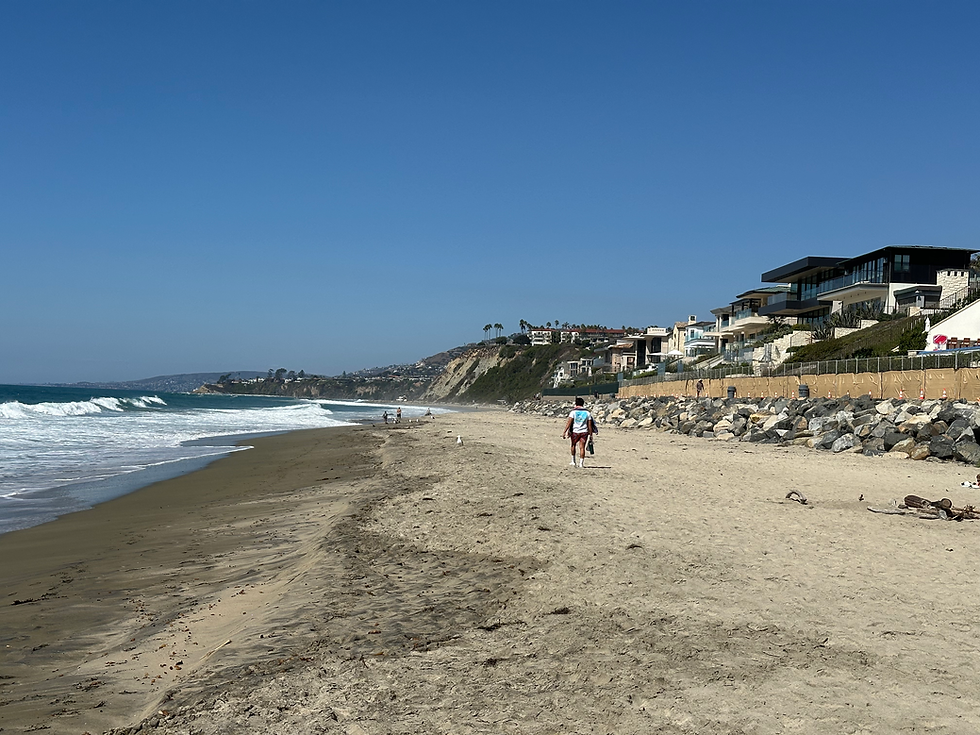 Person walking on a Coastal Orange County beach with luxury homes on the bluffs overlooking the Pacific Ocean