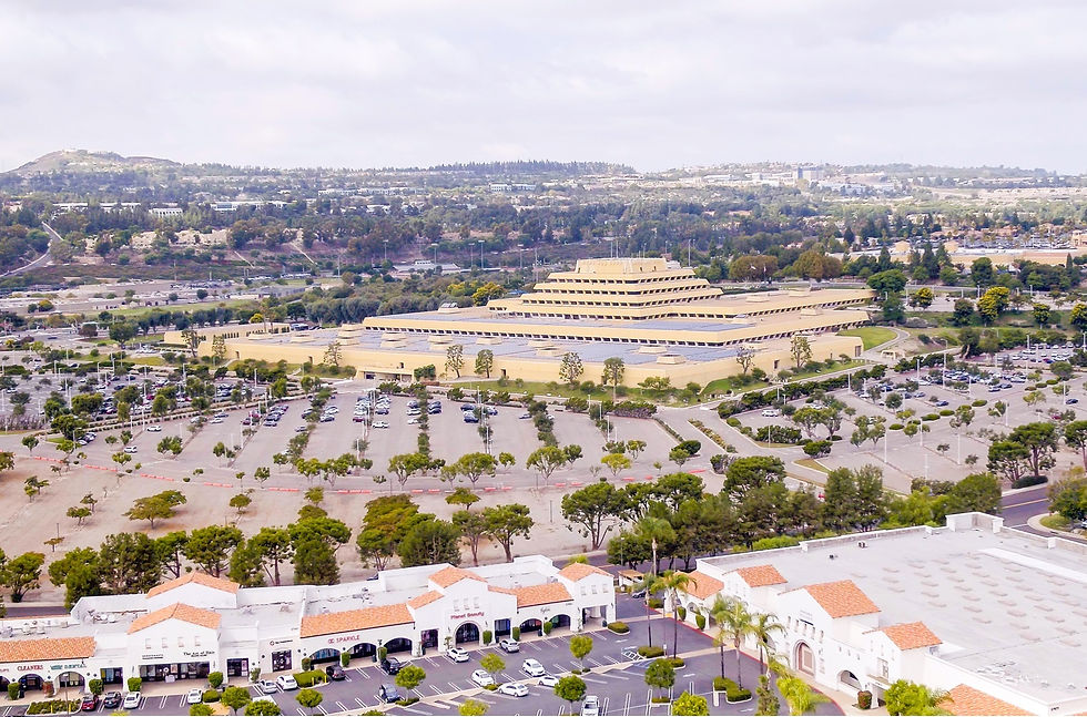 Aerial view of the Ziggurat building in Laguna Niguel, California, surrounded by a large parking lot and nearby retail centers, with residential and hillside areas in the background.