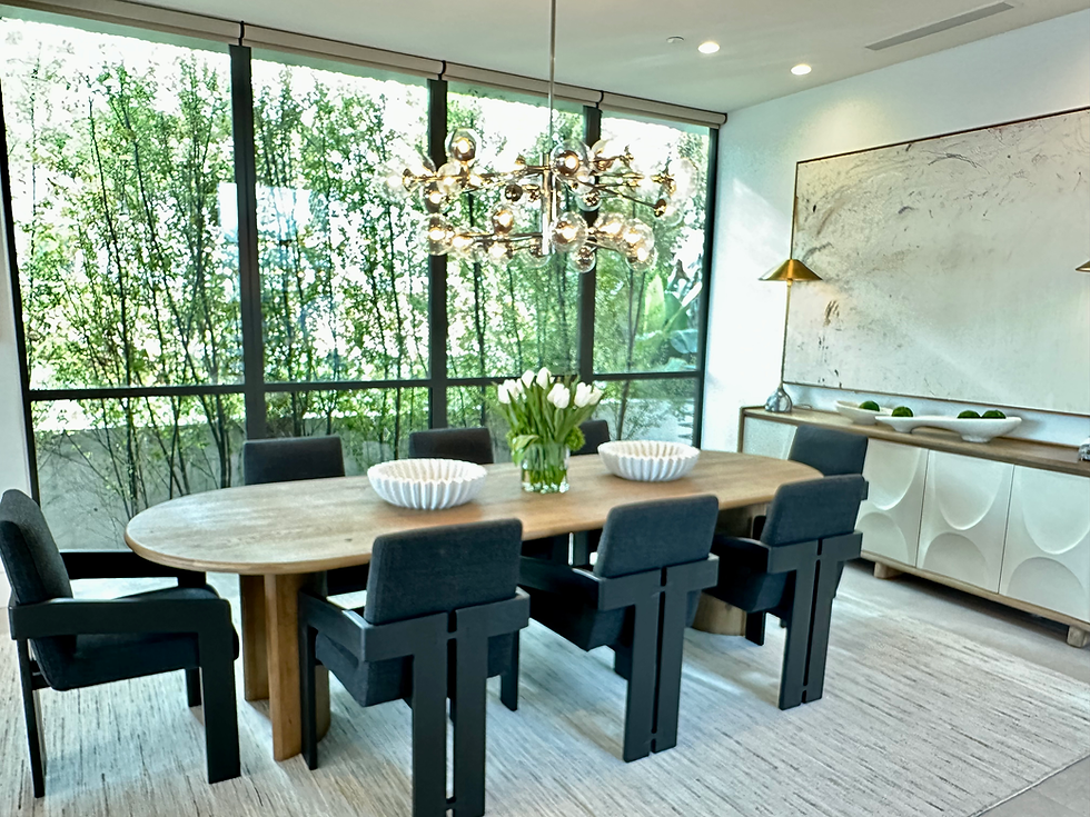 Modern dining room with a long wood table, eight black upholstered chairs, a sculptural glass chandelier, and large windows showcasing lush greenery outside.