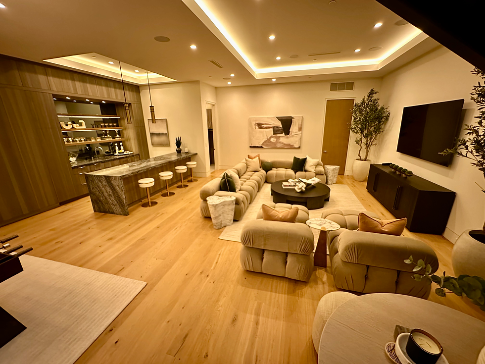 Modern luxury living room with warm recessed lighting, a plush sectional sofa, elegant decor, and a built-in bar with marble countertops and open shelving.