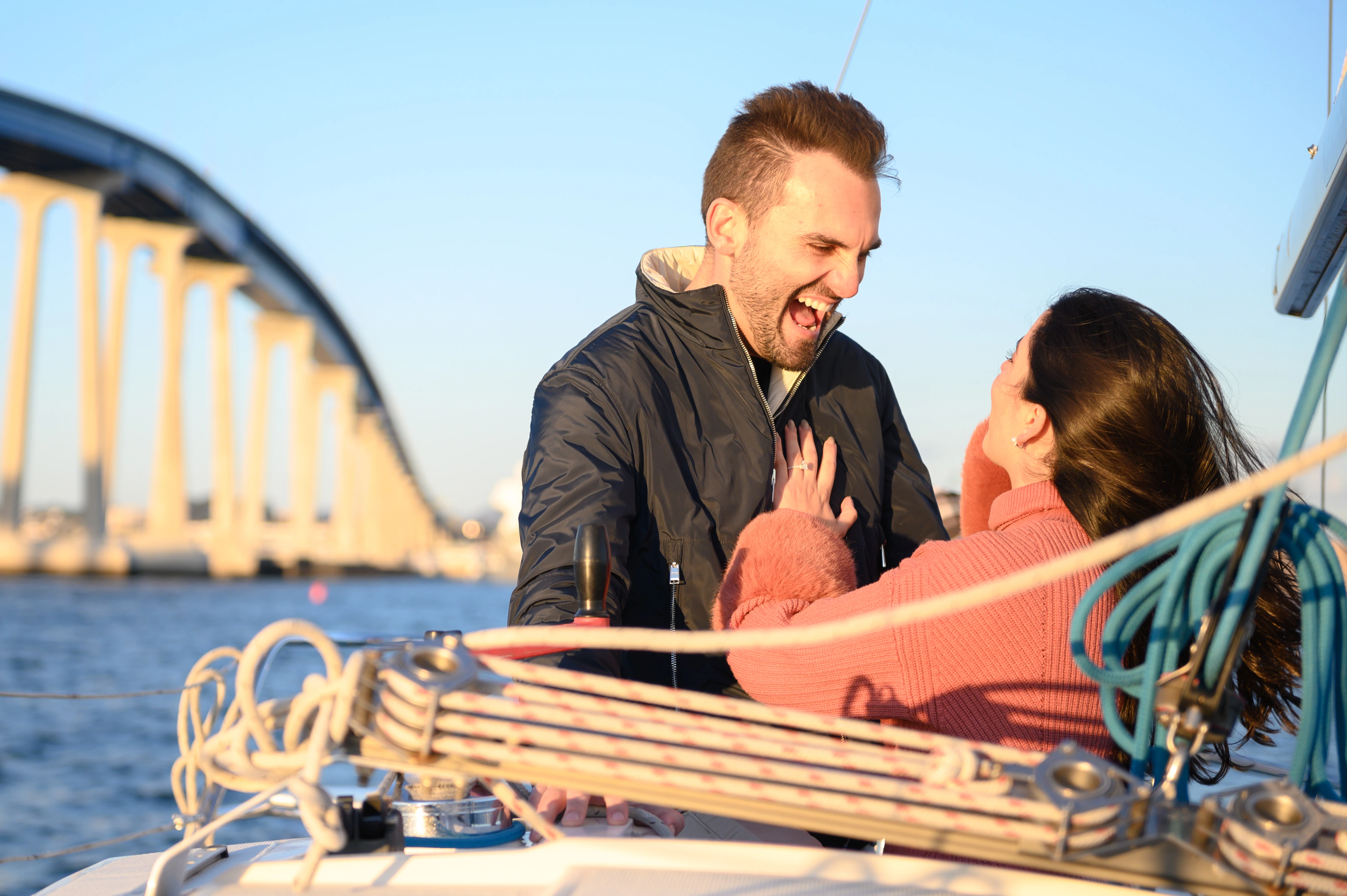 Engaged couple celebrating a romantic proposal on a sailboat near the Coronado Bridge in San Diego. Best San Diego proposal photographer.