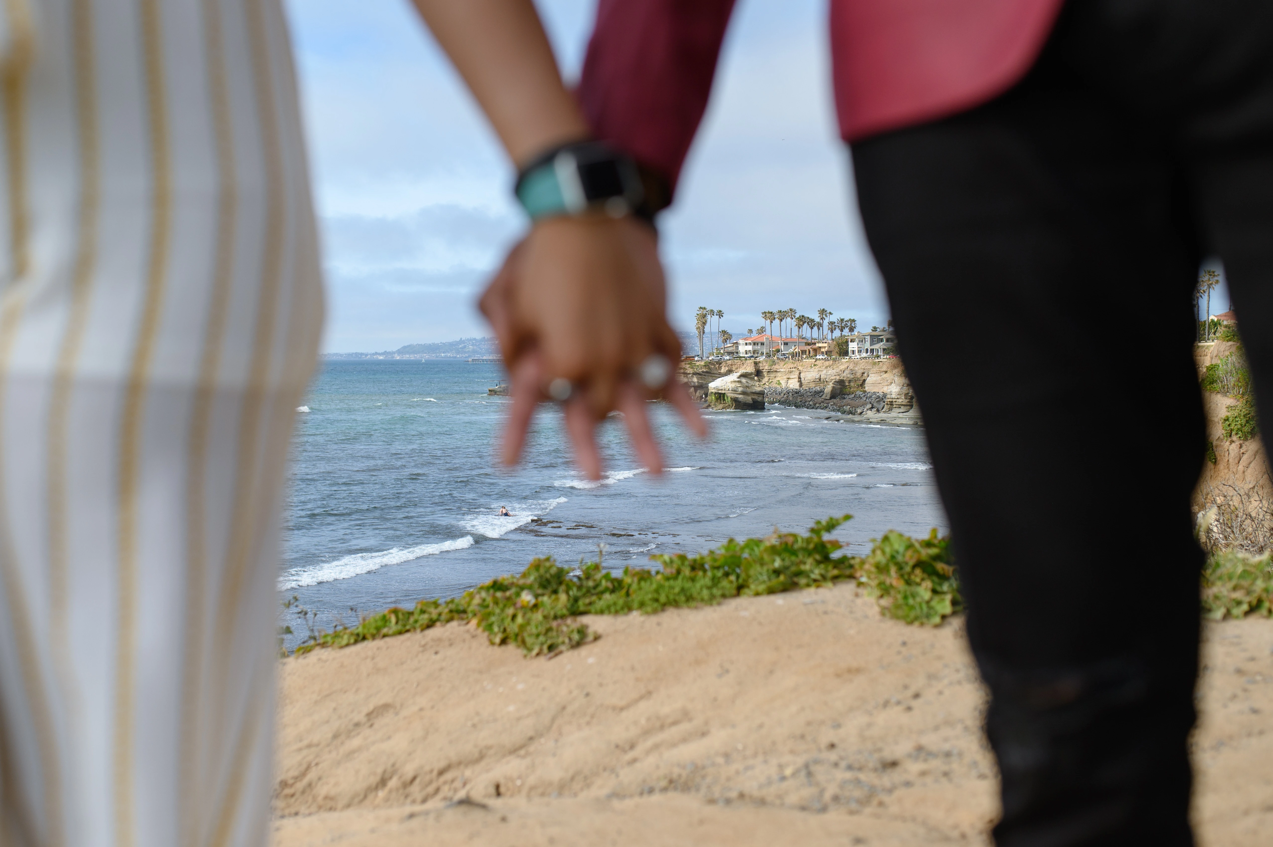 Hands intertwined with the ocean in the background at Sunset Cliffs, symbolizing unity and romance. Best San Diego proposal photographer captures the intimate details of planning a surprise proposal.