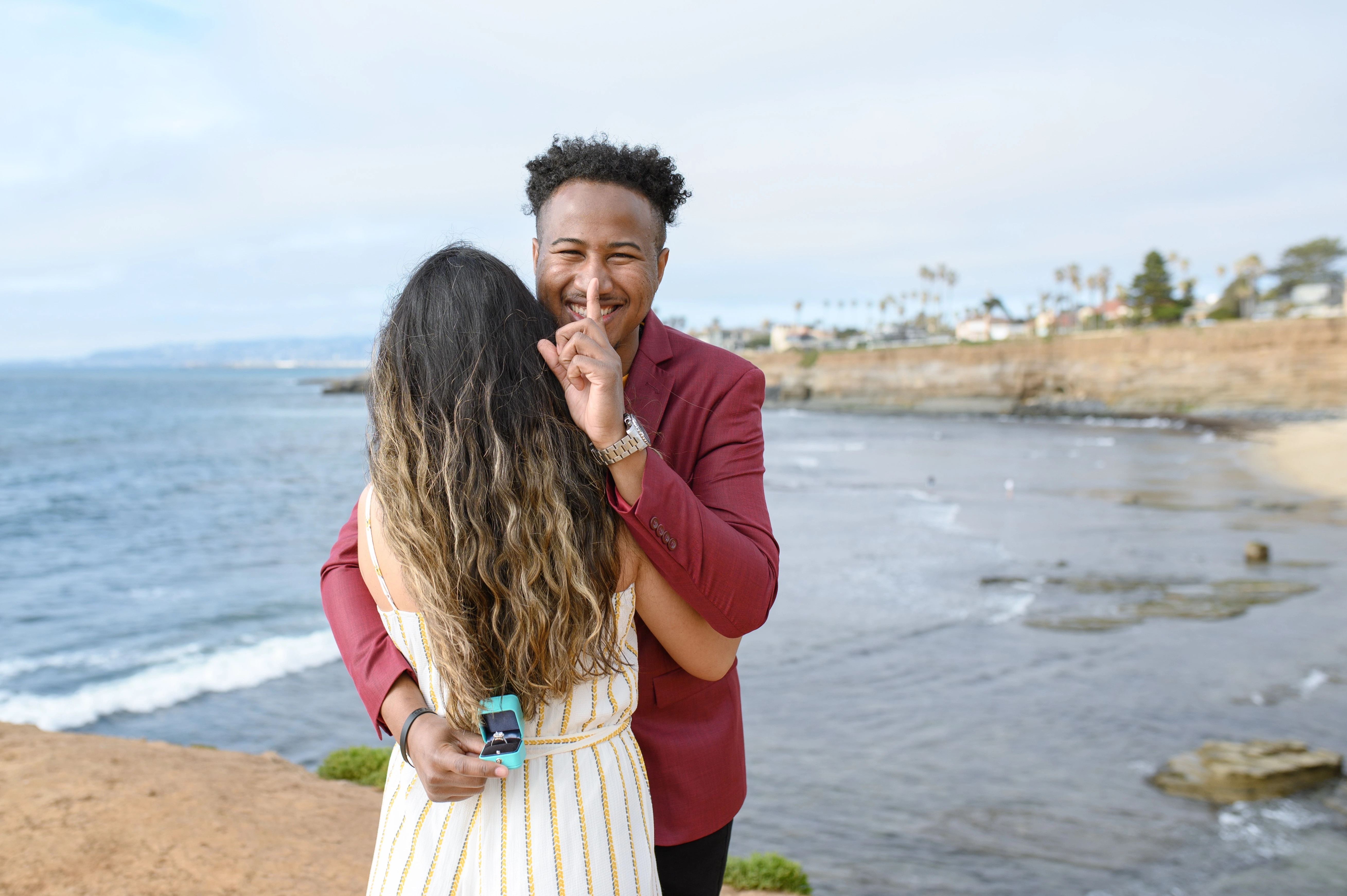 San Diego proposal photographer captures a couple at Sunset Cliffs, with the man preparing to propose, embodying the essence of planning a surprise proposal.