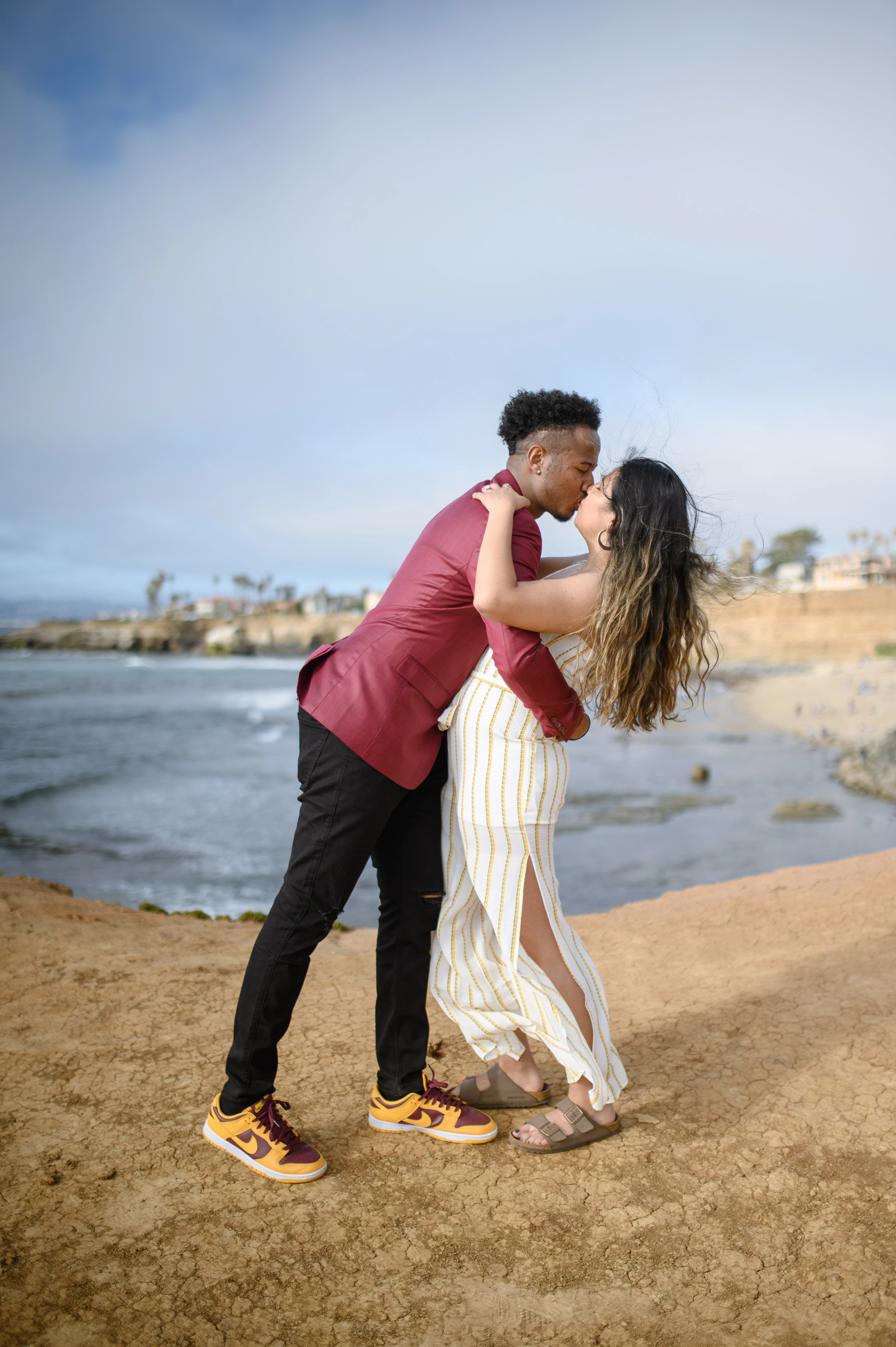 An affordable San Diego proposal photographer captures a couple sharing a loving moment at Sunset Cliffs, highlighting the joy of engagement and the stunning coastal scenery.