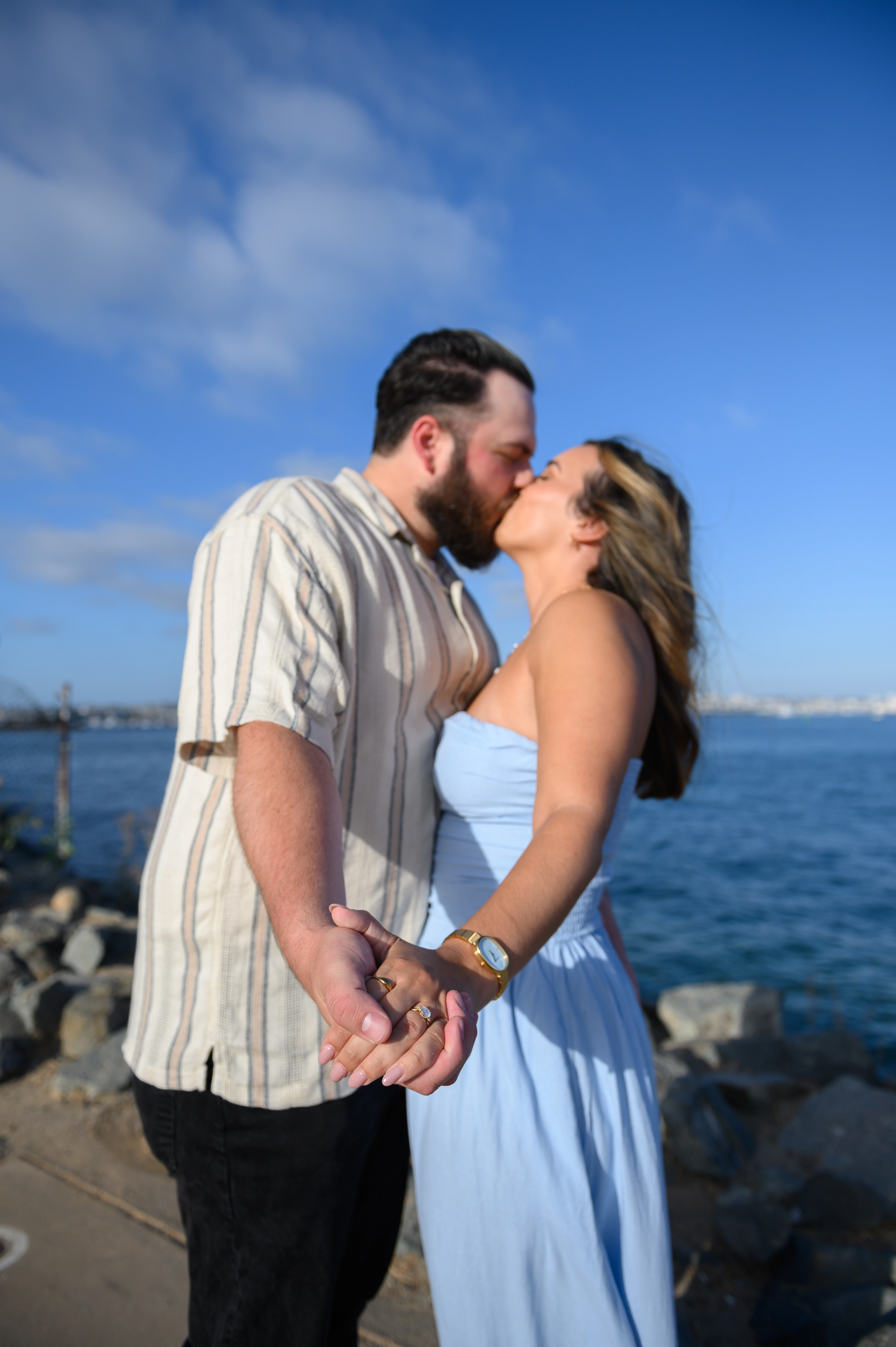 Best San Diego proposal photographer captures a couple holding hands, showcasing their love and engagement against the stunning backdrop of the San Diego coastline.