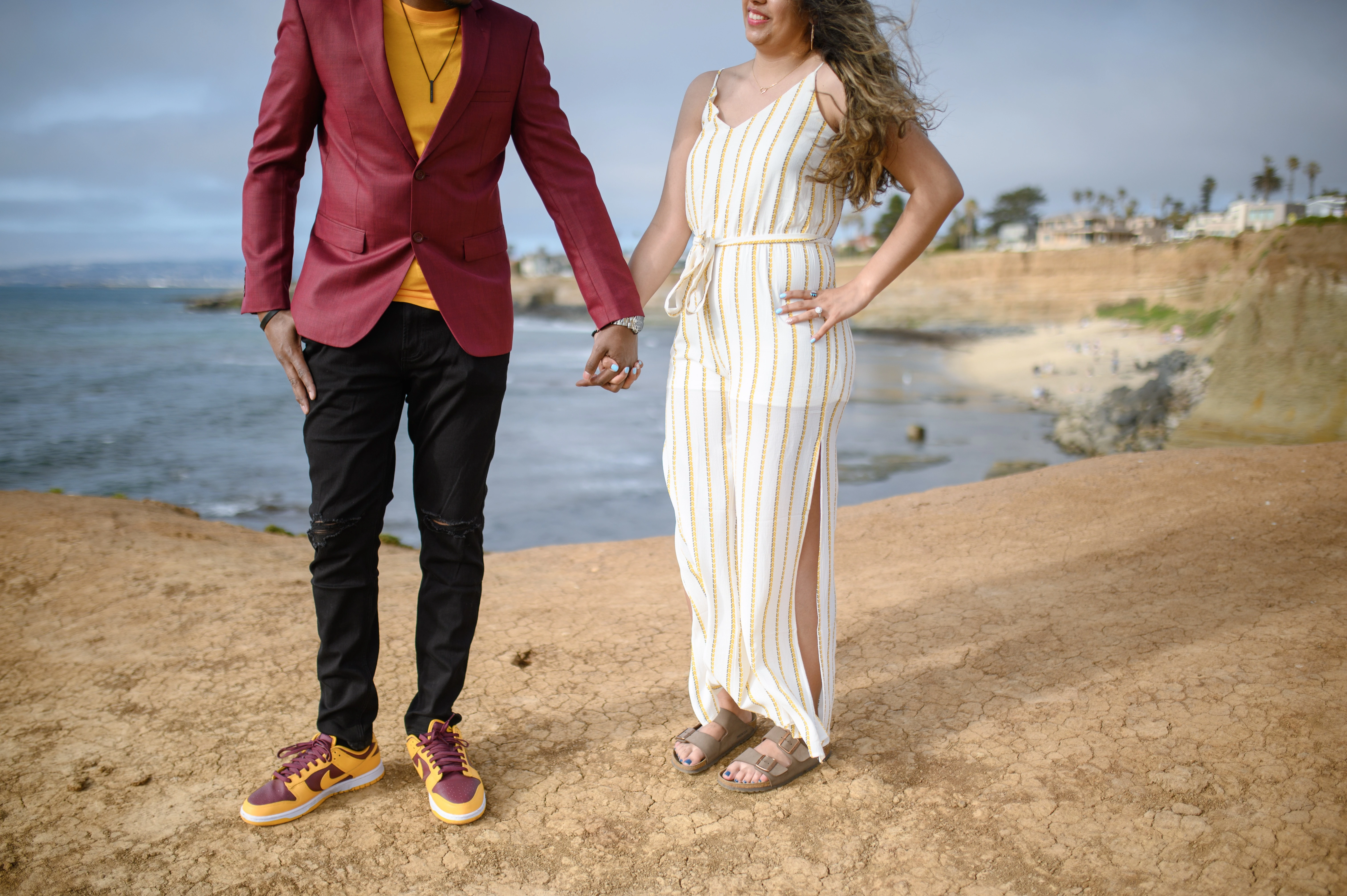 Engaged couple standing together on a cliff at Sunset Cliffs overlooking the ocean, highlighting the beauty of San Diego. Affordable San Diego proposal photographer captures this romantic engagement moment.